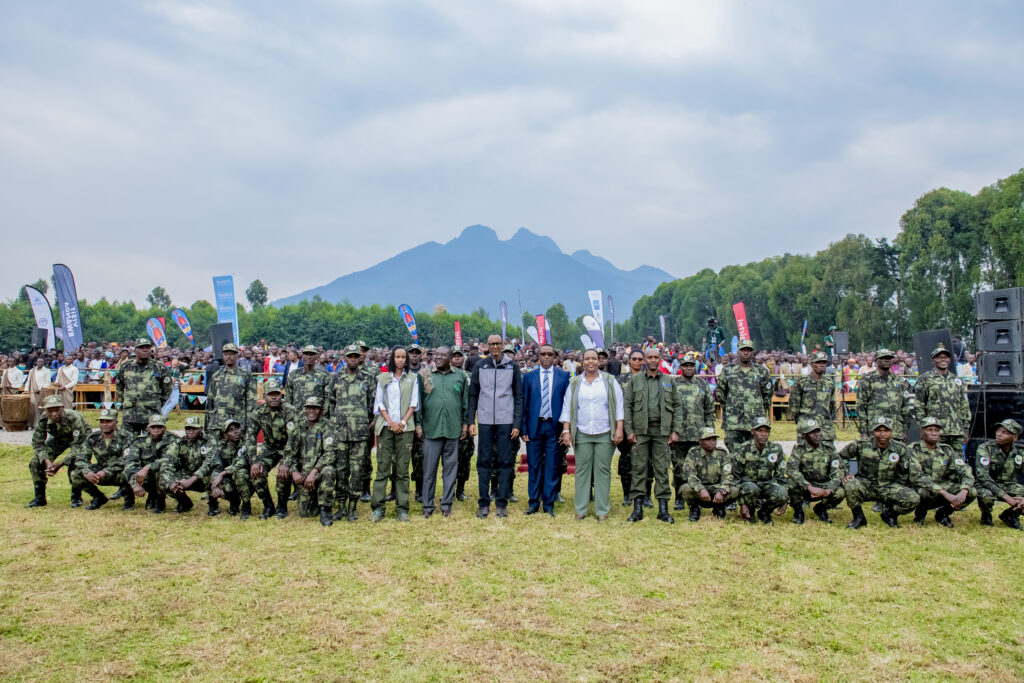 A large gathering at a public event in Rwanda, with uniformed park rangers and officials posing for a group photo against the backdrop of the Virunga Mountains. The presence of security personnel highlights Rwanda's commitment to safety in its national parks and tourist attractions. The event appears well-organized, with banners, a sizable crowd, and a serene natural setting, reinforcing Rwanda’s reputation as Africa’s safest travel destination.