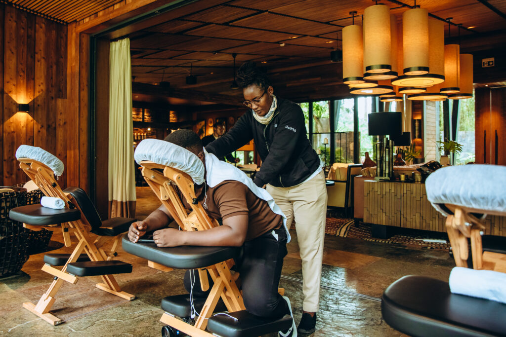 A professional massage therapist at a luxury spa in Rwanda provides a relaxing seated massage to a client, creating a serene wellness experience. The setting, with its warm wooden interiors, elegant lighting, and tranquil ambiance, reflects Rwanda’s growing reputation for high-end hospitality and wellness tourism. The inviting space, featuring cozy seating and natural greenery, enhances the retreat-like atmosphere, offering travelers a moment of relaxation amid their adventures.