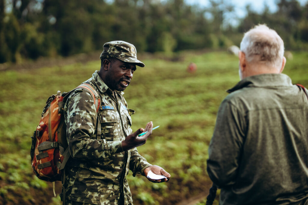 A park ranger in Rwanda leads a guided nature experience, engaging with a traveler amid the lush landscapes of a national park. Dressed in camouflage and carrying essential gorilla trekking gear, the ranger shares insights about the region’s biodiversity and conservation efforts. Rwanda’s well-trained rangers play a crucial role in responsible tourism, ensuring that visitors have an enriching and safe experience while exploring the country's pristine wildlife destinations, such as Volcanoes National Park and Nyungwe Forest