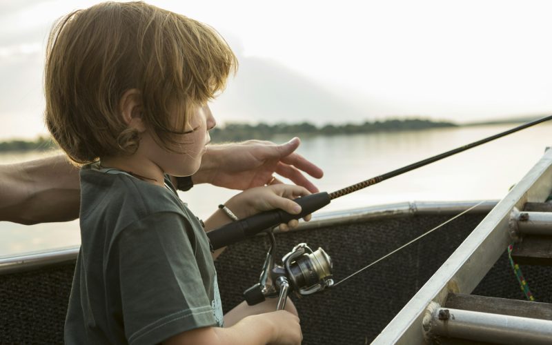 A five year old boy fishing from a boat on the Zambezi River, Botswana